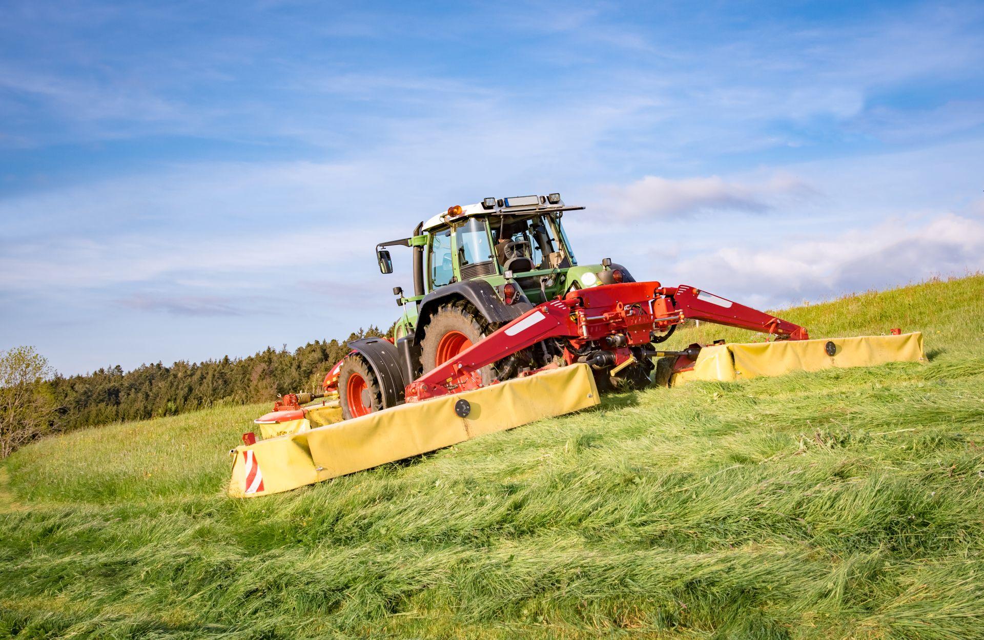 Grosser Traktor mit angebautem Maehwerk bei der Pflege einer weiten Gruenflaeche